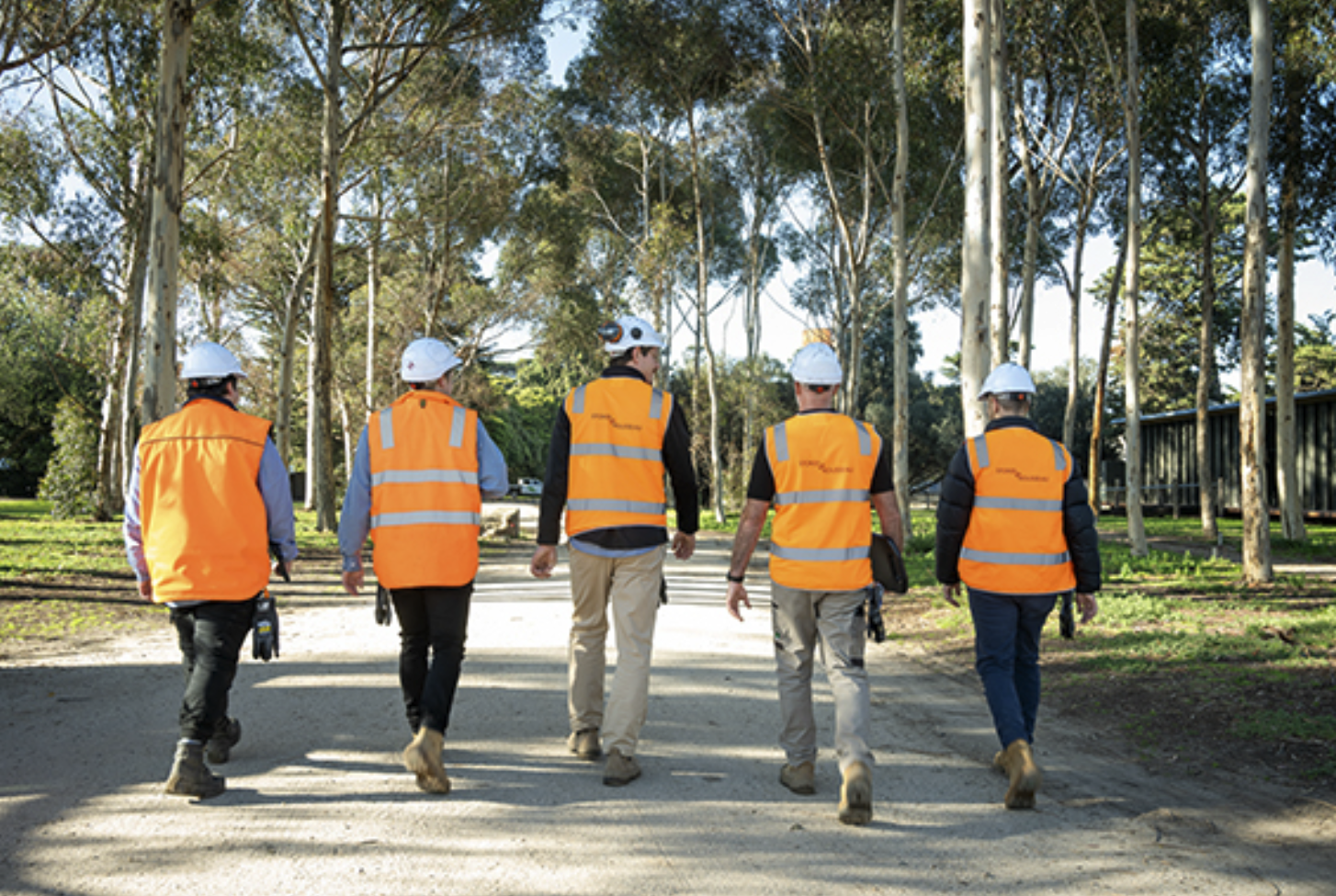 Five Stokes team members walking together along a tree-lined site path